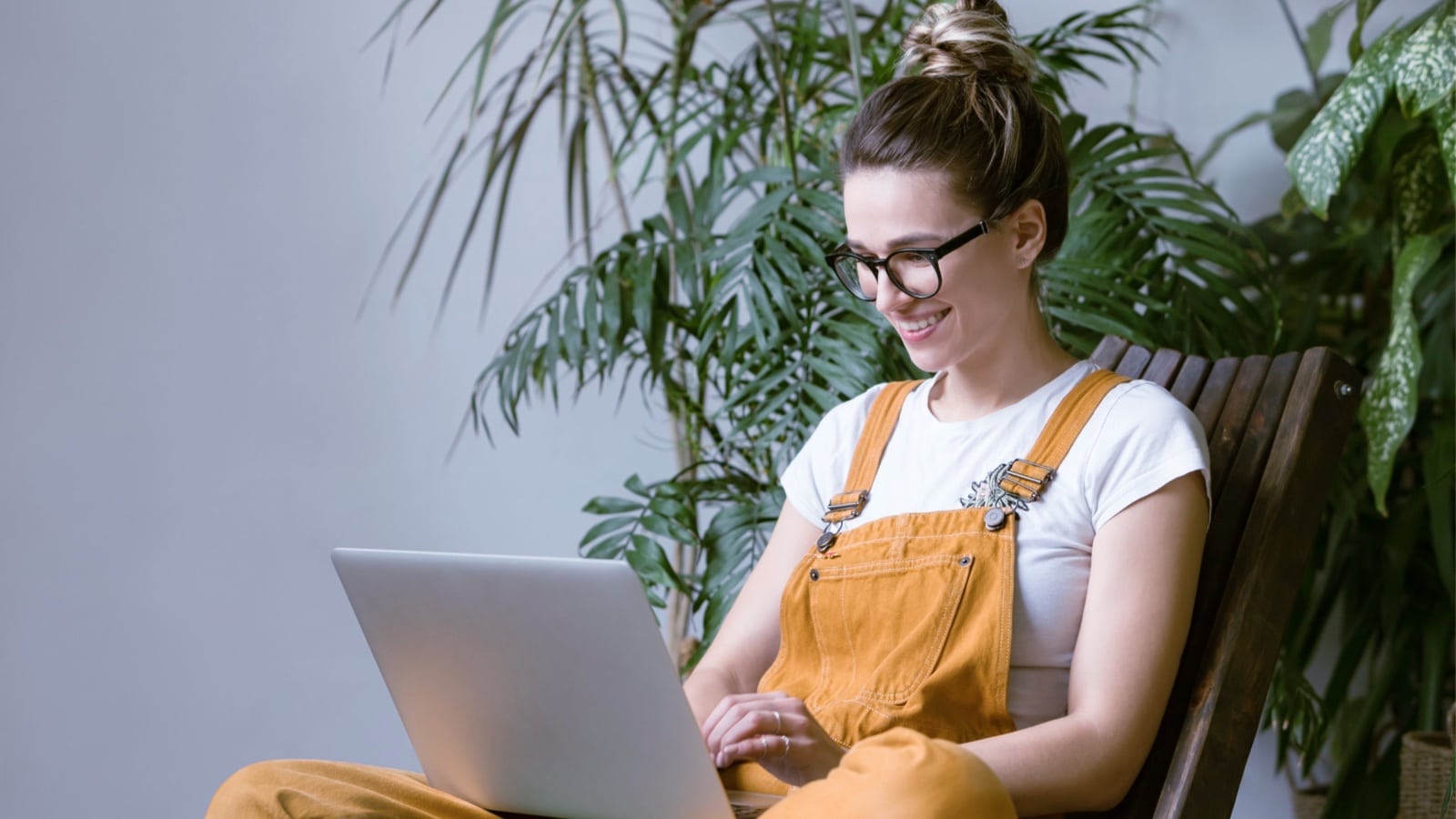 Eine Frau arbeitet neben einer grossen Pflanze an ihrem Laptop.