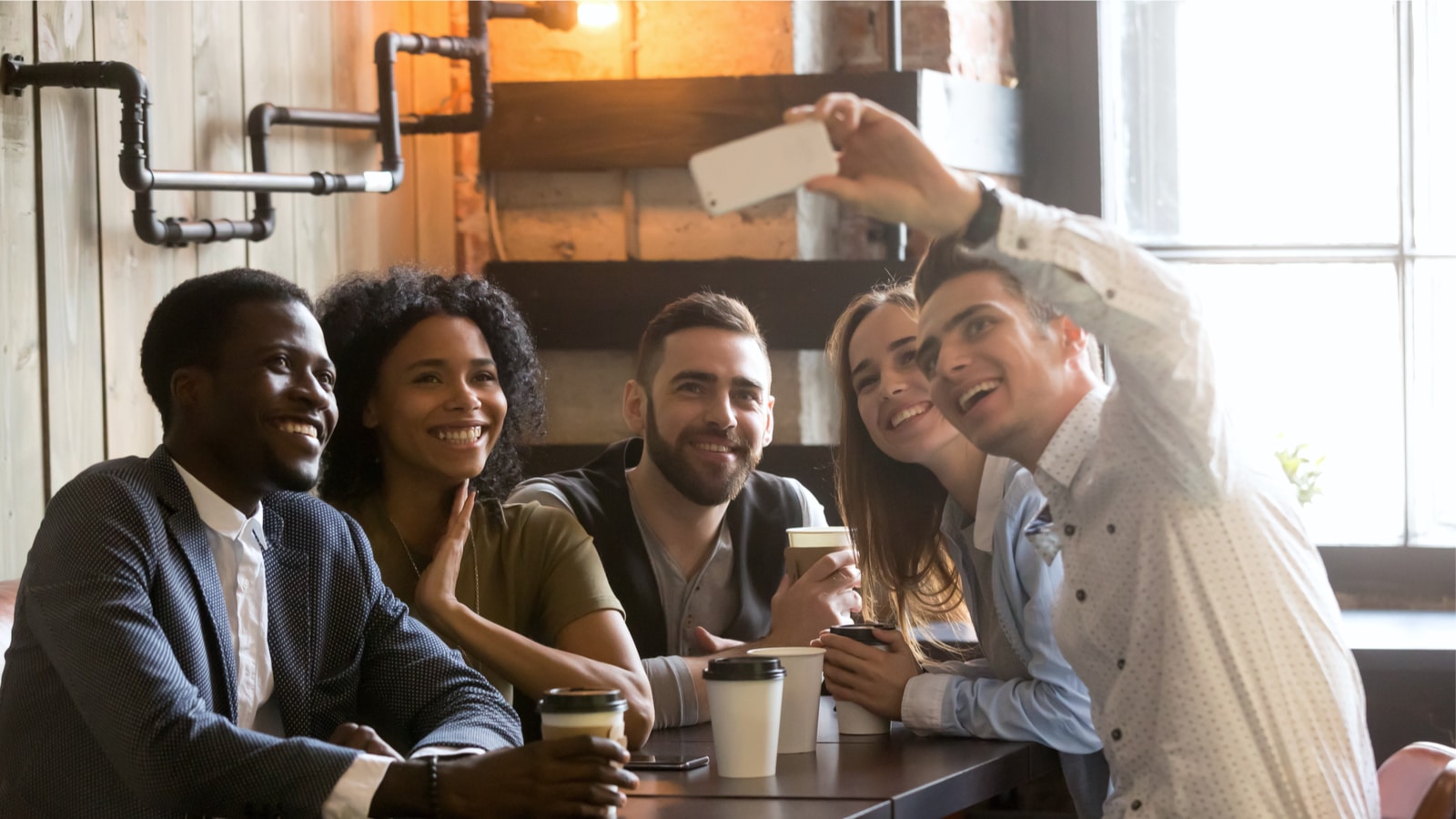 Eine Gruppe diverser Millennials schiesst ein Gruppenfoto mit einem Smartphone.