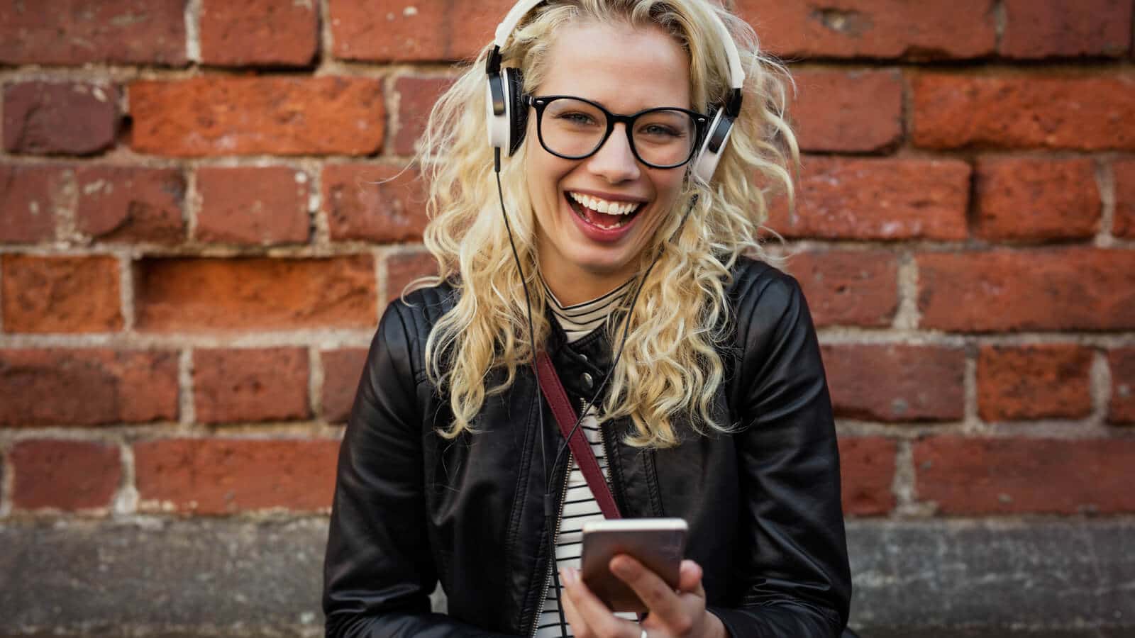 Eine lachende Frau hört Musik auf ihrem Smartphone auf Spotify.
