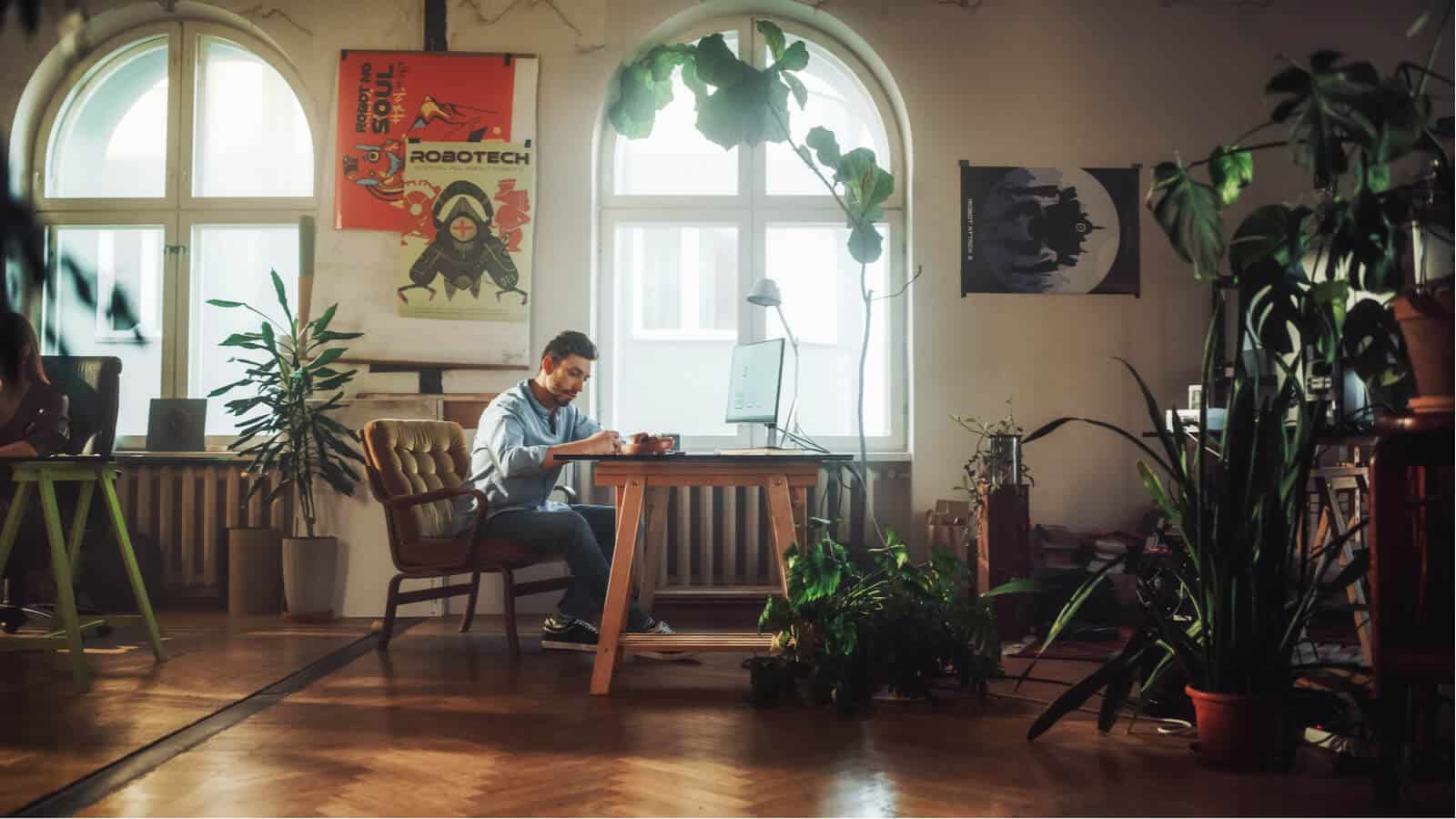 Mann arbeitet am Laptop in Büro voll mit Pflanzen.