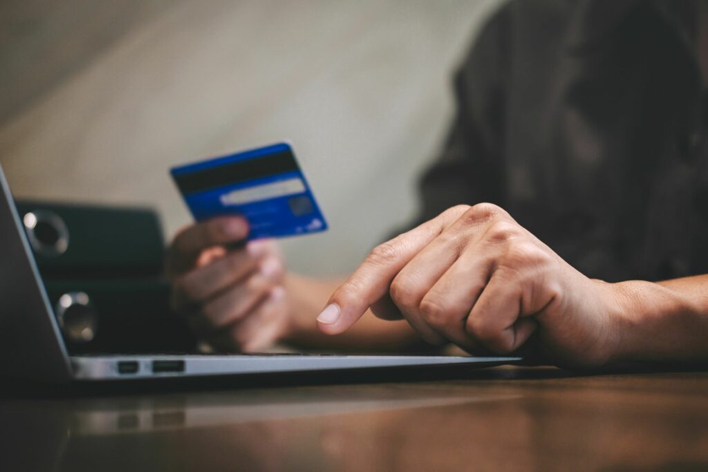 Eine Person sitzt mit Kreditkarte in der Hand vor dem Laptop.