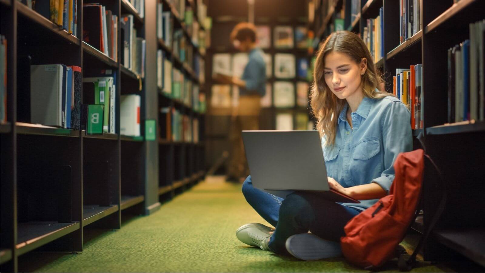 Junge Studentin schreibt ihre Marketing Bachelorarbeit am Laptop in der Bibliothek