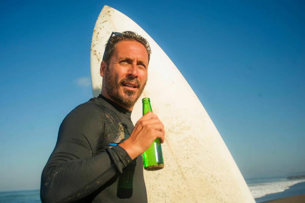 Ein Mann mit einem Surfbrett und einem Bier in der Hand.