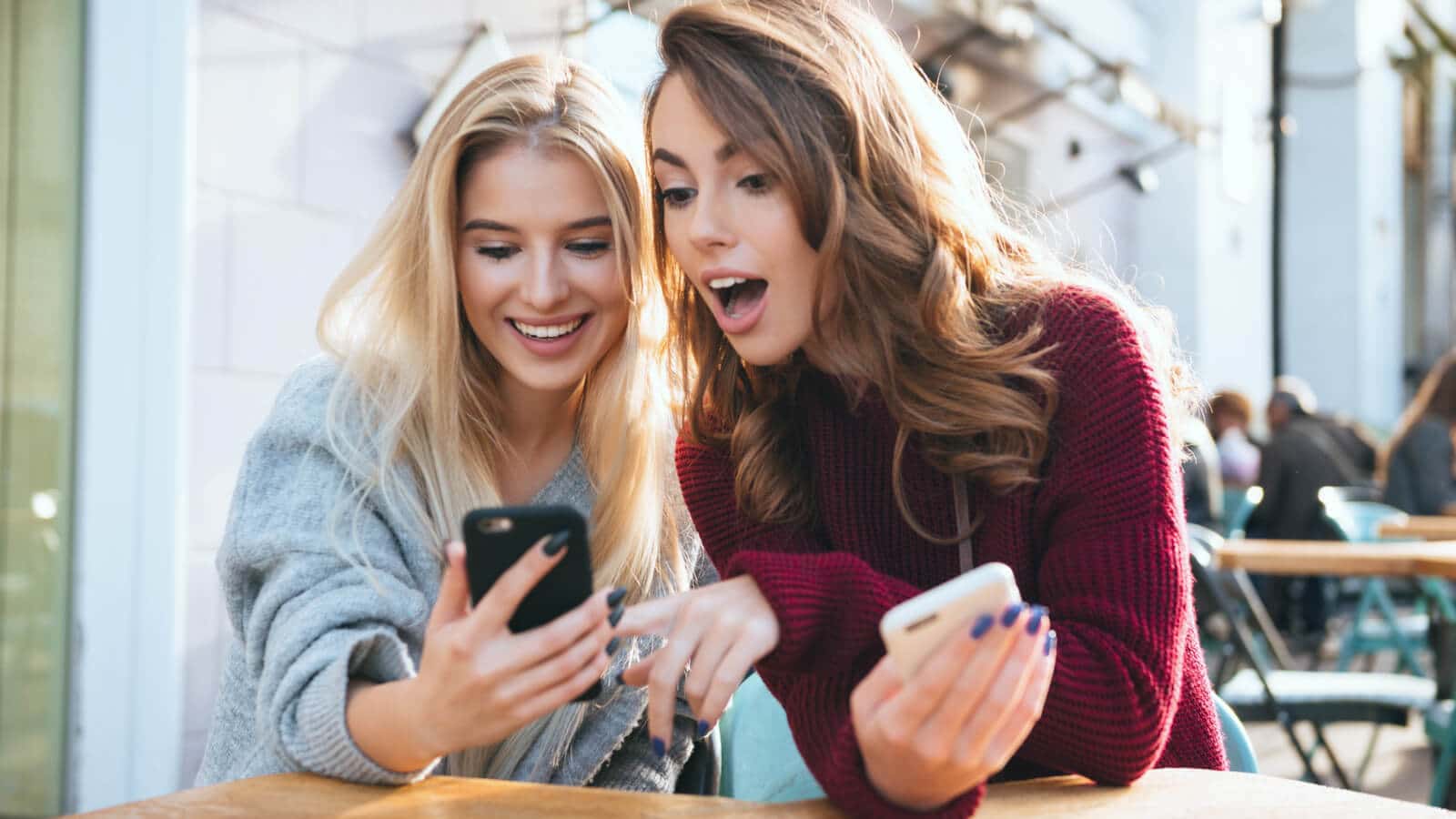 Zwei Frauen schauen auf ihren Smartphones TikToks und Reels um zu schauen, welche Videos besser sind.