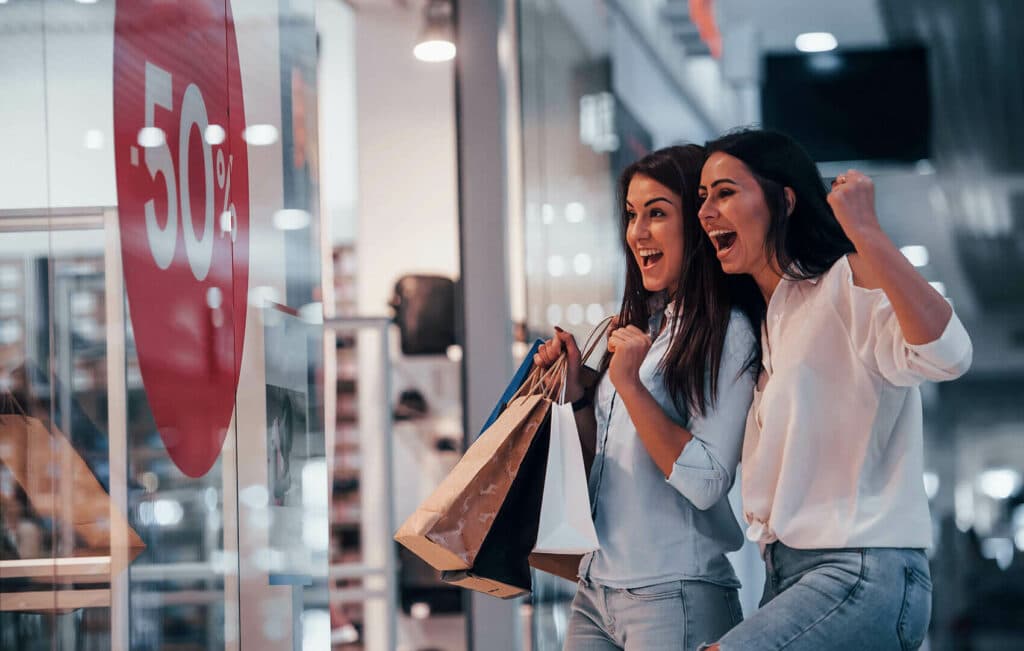 Zwei Frauen beim Shopping vor einer 50% Sale Tafel.