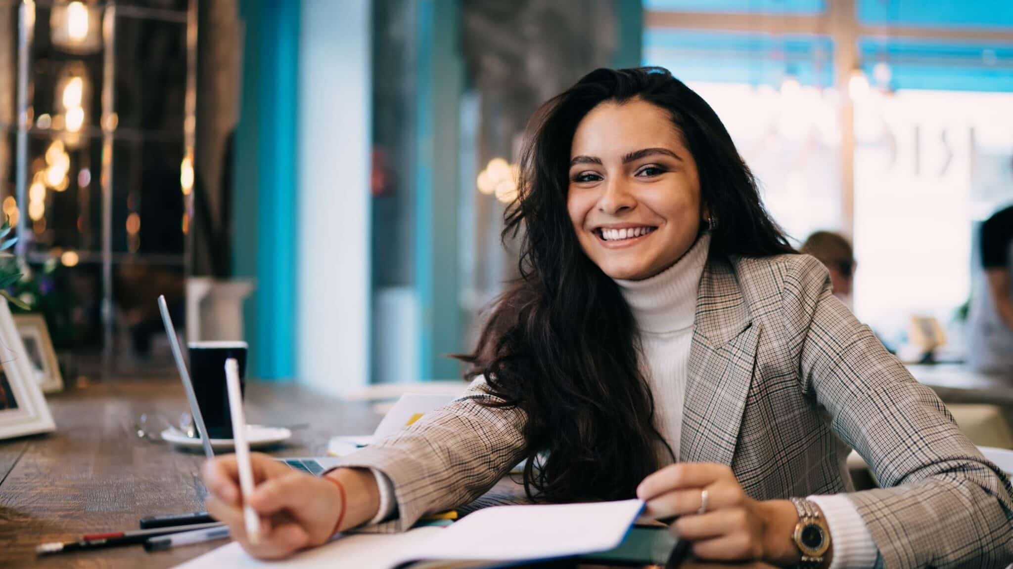 Porträt einer Frau, die während der Prüfungsvorbereitung im öffentlichen Café in die Kamera lächelt.