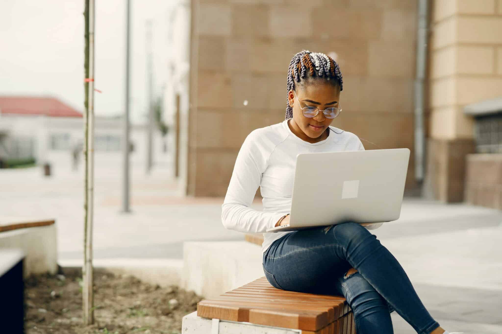 Eine Frau sitzt auf einer Bank mit einem Laptop auf dem Schoss.